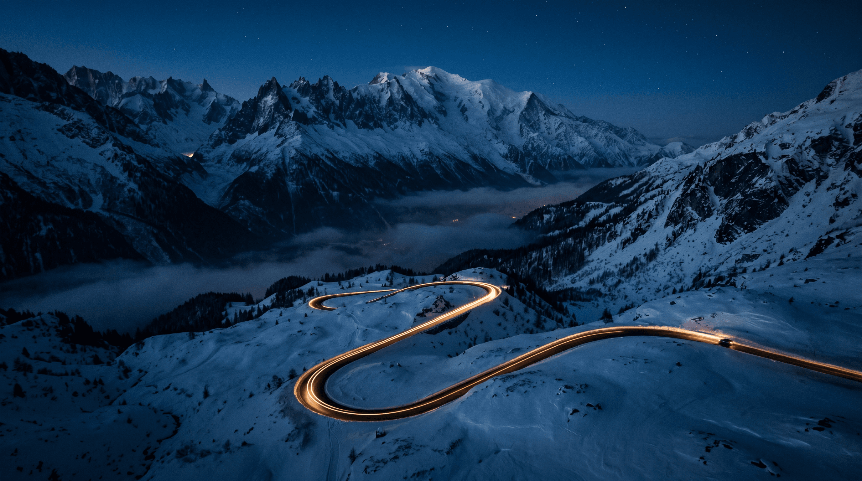 Winding mountain road at night beneath snow-capped peaks